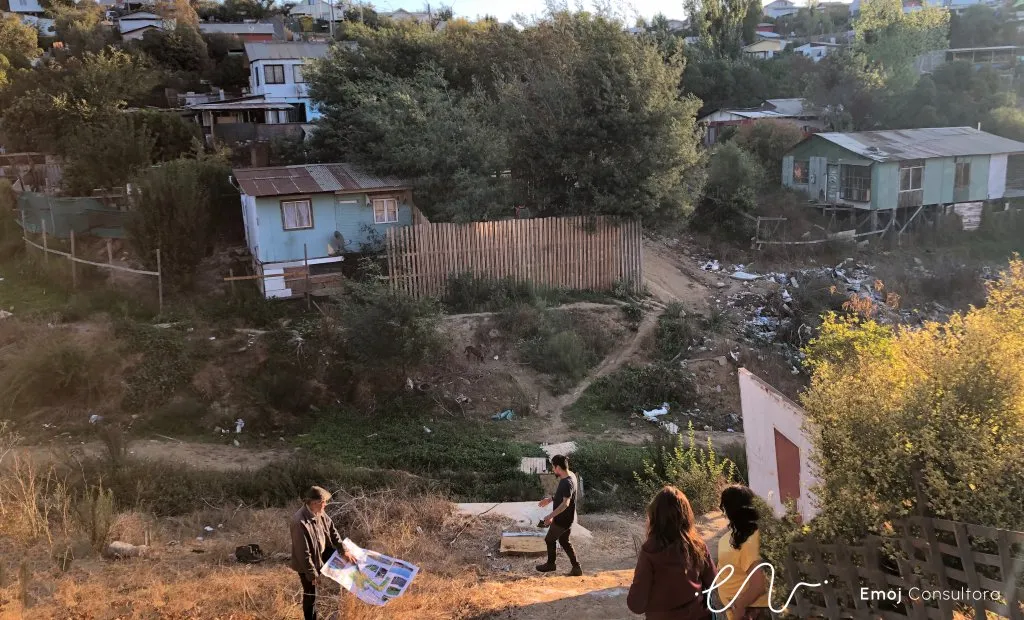 Equipo de EMOJ revisando planos en un sitio eriazo en ladera de Quilpué, rodeado de viviendas.