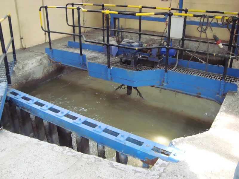 Canal de una planta de tratamiento de aguas servidas con pasarelas y compuertas metálicas azules.