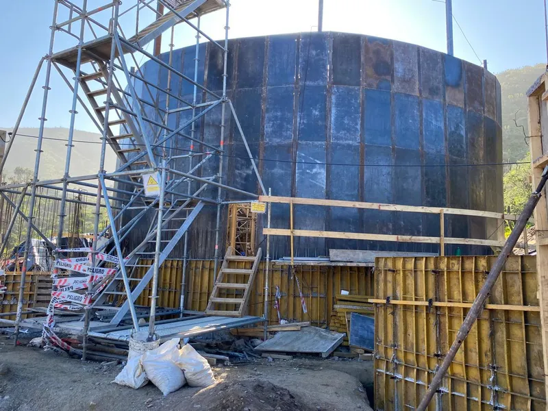 Estanque metálico de agua potable en construcción, rodeado de andamios y moldajes.