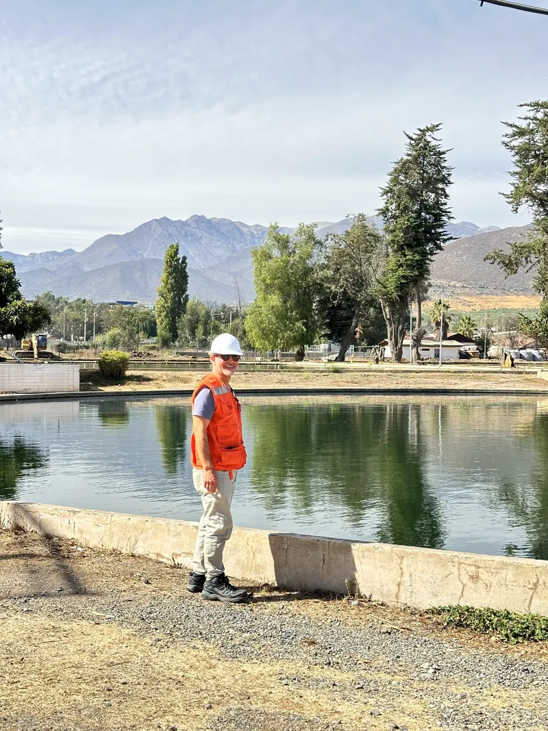 Profesional de EMOJ con casco y chaleco reflectante junto al Canal La Petaca, con la cordillera al fondo.