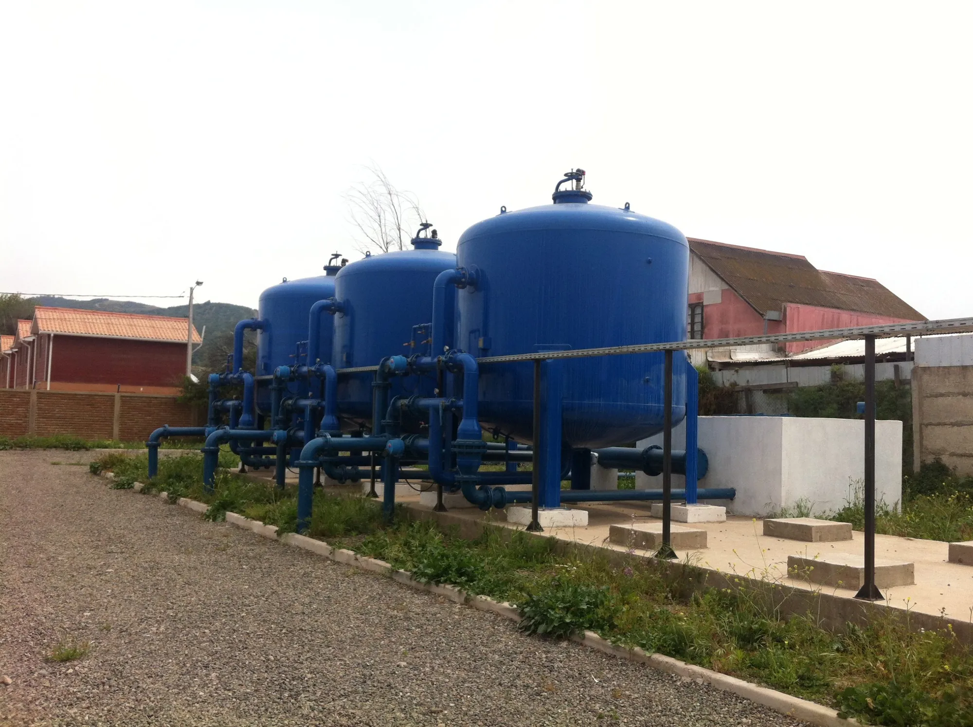 Tres estanques azules de una planta de agua potable conectados por tuberías.