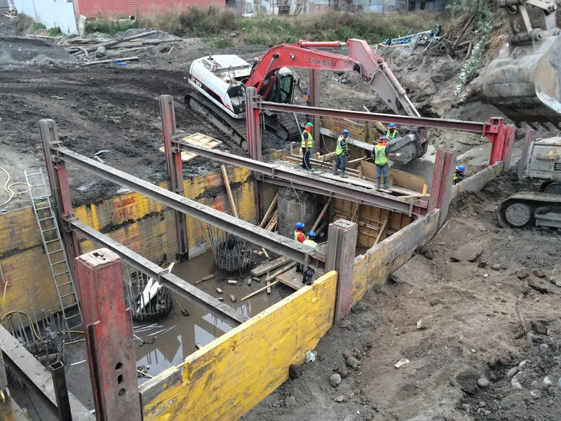 Excavación entibada con una excavadora y trabajadores con casco durante la construcción del puente Llollito.