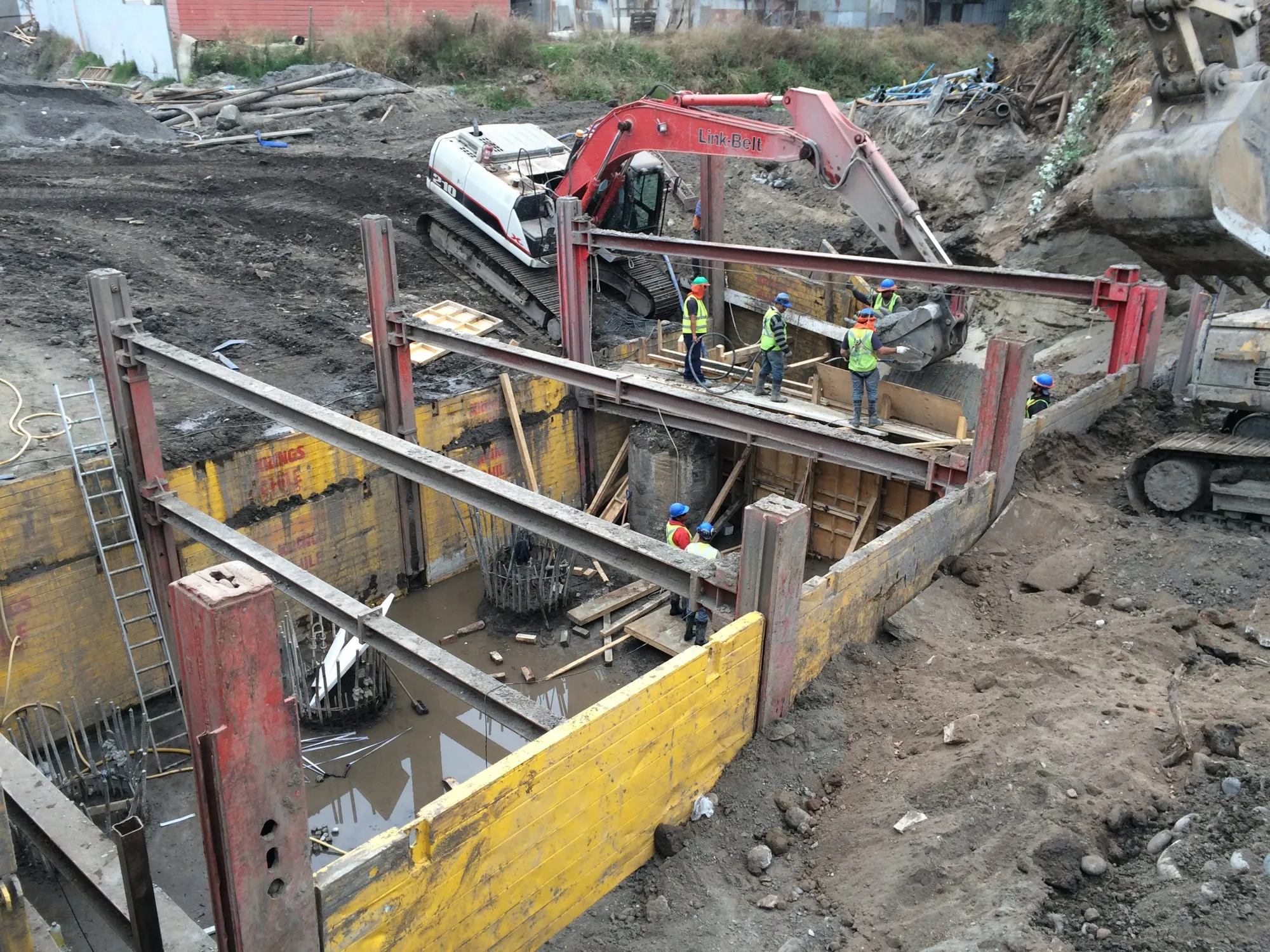 Excavación entibada con una excavadora y trabajadores con casco durante la construcción del puente Llollito.