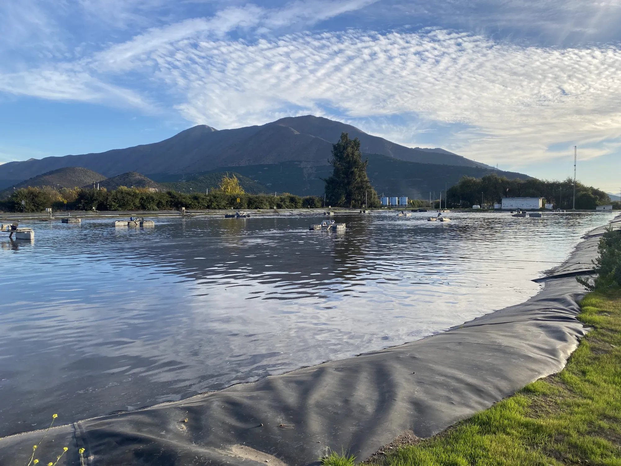 Laguna de estabilización revestida con geomembrana, con cerros al fondo.