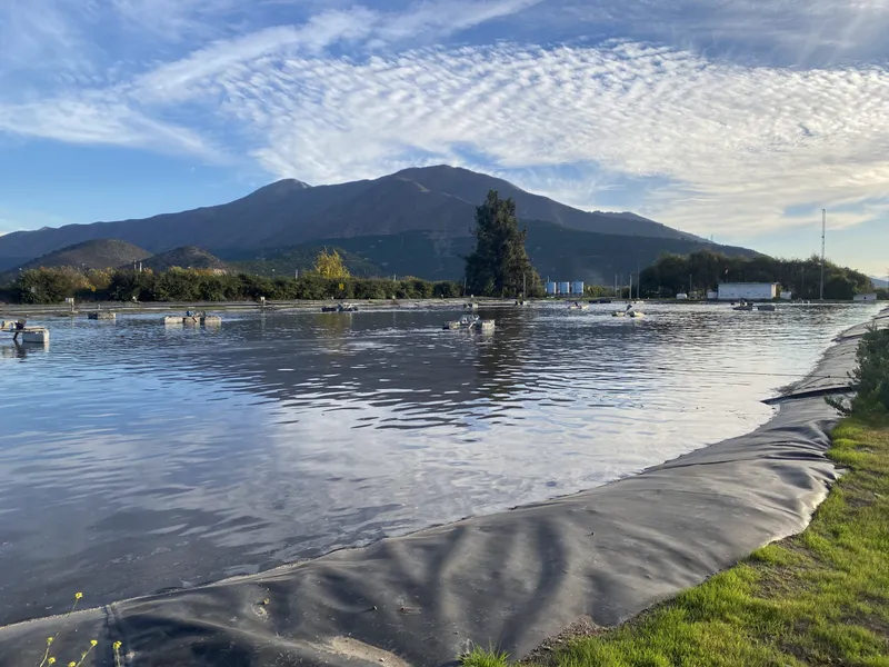 Laguna de estabilización revestida con geomembrana, con cerros al fondo.